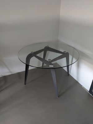 une table en verre avec un piètement en métal, placée dans un coin