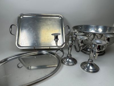Plusieurs objets plaqués argent sont posés sur une surface blanche