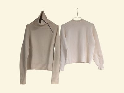 pair of white sweaters hanging on a hanger on a white wall