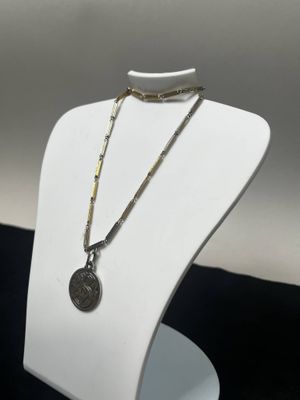 un mannequin blanc portant un collier sur lequel est accrochée une pièce de monnaie