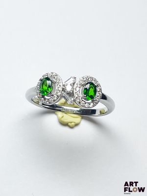 un gros plan d'une bague sertie d'un diamant vert et blanc posée sur une surface blanche