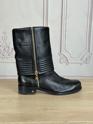 une paire de bottes en cuir noir avec des fermetures éclair, posée sur une table en bois
