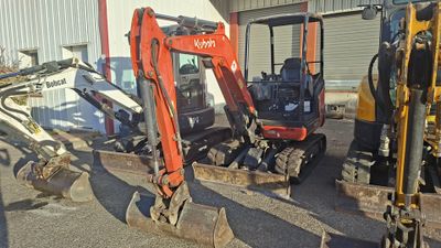two small excavators parked next to each other in front of a building