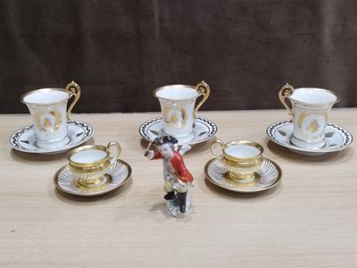 cinq tasses et soucoupes posées sur une table, avec une figurine représentant un homme