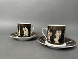 two cups and saucers with black and gold designs on them