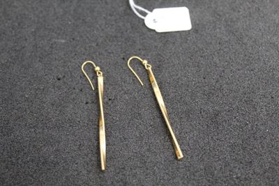 une paire de boucles d'oreilles en or posée sur une table, à côté d'une étiquette