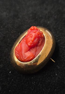 une image représentant une broche rouge et dorée avec le visage d'un homme
