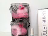 a pink stuffed duck sitting in a bucket next to a bottle of perfume