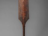 an old wooden paddle on a metal stand against a gray background
