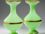 une paire de vases en verre vert aux bords dorés, posés sur une surface blanche