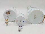 two white porcelain vases with gold trim and a small figurine