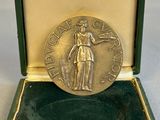 une image représentant une médaille d'or dans un coffret vert posé sur une surface blanche