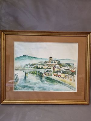 framed watercolor painting of a village by a river in a gold frame
