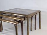 three brass nesting tables with glass tops on a white background
