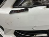 the front end of a white car with a number plate on it