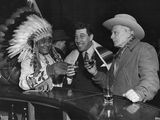 black and white photo of a man in a feathered headdress talking to a man in a suit and tie