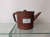a brown teapot on a glass shelf with a label on it