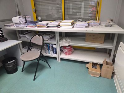 un bureau encombré de papiers et une chaise dans un coin