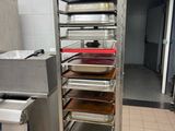 several trays of food are stacked on a metal rack in a kitchen