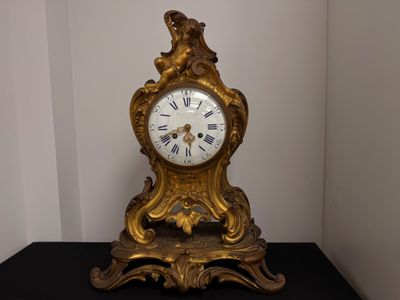 une horloge dorée posée sur une table noire, avec un mur blanc en arrière-plan