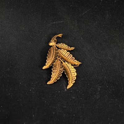 un gros plan d'une broche en feuille d'or posée sur un tissu noir