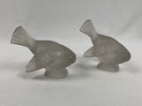 une paire de figurines d'oiseaux en verre posées sur une surface blanche