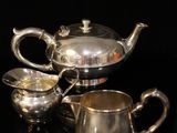 two silver teapots and a sugar bowl on a black surface