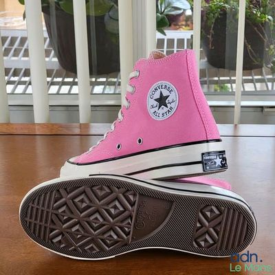 Des Converse roses sont posées sur une table en bois, avec une plante en arrière-plan