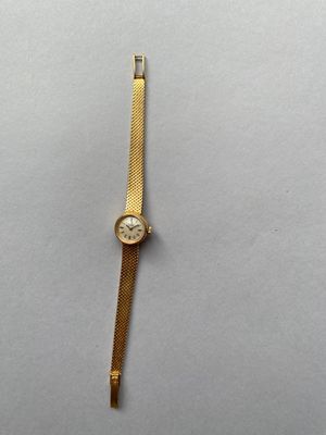 gros plan d'une montre en or sur une surface blanche