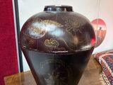 un vase noir posé sur une table en bois, avec un mur rouge en arrière-plan