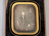 une vieille photo d'un homme en costume, assis sur une chaise
