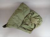 a green sleeping bag on a white surface next to a pillow