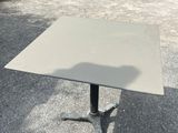 a square table with a metal base in the middle of a parking lot