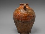 un vieux vase marron portant une inscription, posé sur une surface grise