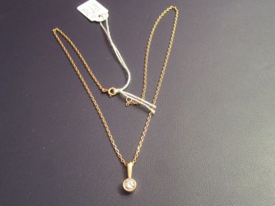 two gold necklaces with a white diamond on a black surface