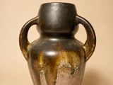 un vase marron muni d'une anse, sur fond beige