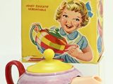a small teapot with a colorful lid next to a box of tea