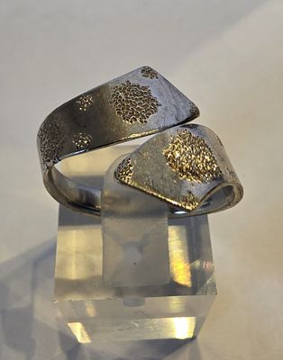 bague en argent parsemée de paillettes dorées, posée sur un bloc de cristal transparent