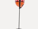 an orange and black sculpture on a black stand on a white surface