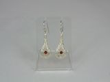 silver earrings with garnets on them on a clear stand