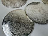 four silver coasters sitting on top of a white table next to each other