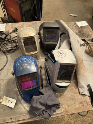 Plusieurs casques de soudage sont posés sur une table dans un atelier