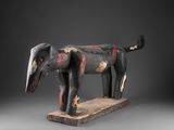 une photo d'une sculpture en bois représentant un chien, posée sur un socle en bois