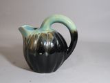 un vase noir et vert posé sur une surface blanche