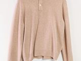 un pull beige suspendu à un cintre sur un mur blanc