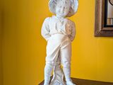 une statue représentant un garçon debout sur une table, devant un miroir