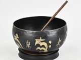 black and gold bowl with chopsticks in it on a white surface