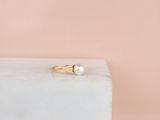 une bague en or ornée d'une perle, posée sur un bloc de marbre blanc