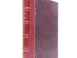 an old book with a red cover sitting on top of a white surface