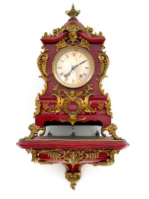 une horloge rouge et dorée posée sur une étagère, sur fond blanc